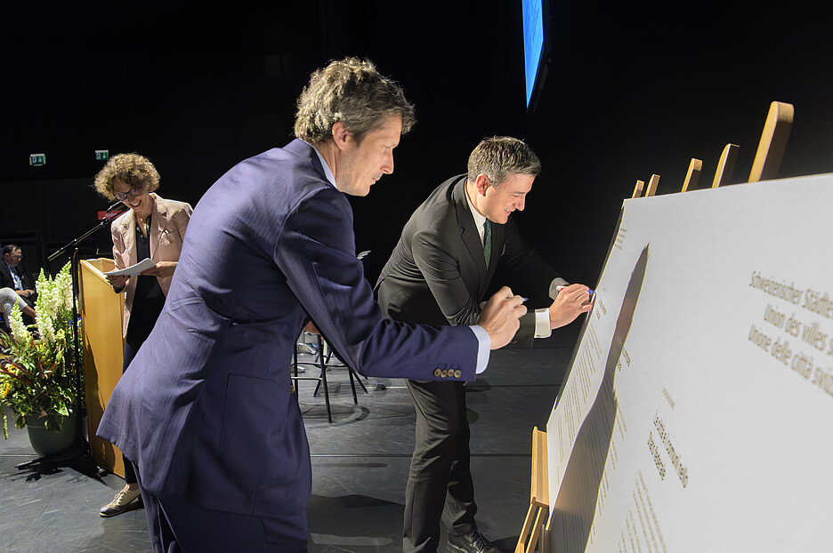 Il presidente dell’ACS Mathias Zopfi (a destra) e Martin Staub del Comune di Vernier firmano la dichiarazione dei comuni e delle città.
